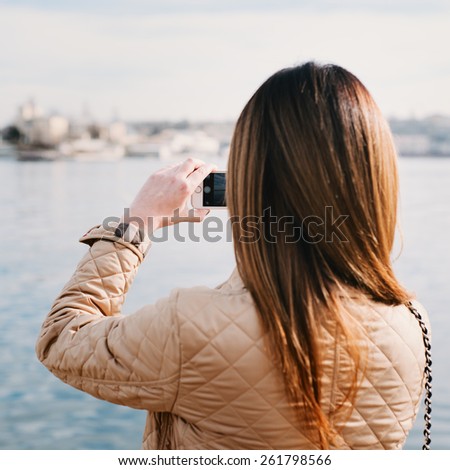 Fashion  woman taking photo with cellphone on the coast on spring. Happy girl on vacation taking picture on sea background. Photo with instagram style filters