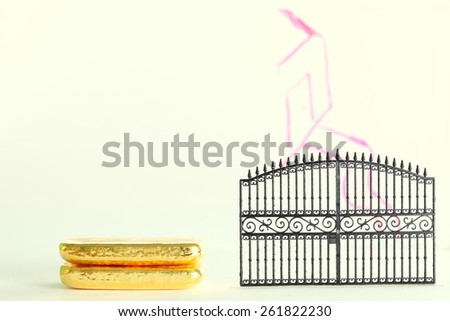 Gold bar beside the plastic gate model in the scene appear the hand drawing house shape on clear acrylic surface represent the mortgage concept idea.