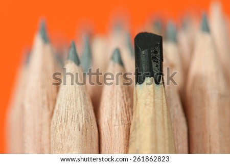 Sketching pencil with thick graphite among a bunch of regular inexpensive wooden drawing pencils on vivid orange background, symbolizing individuality concept, creative design and artistic approach