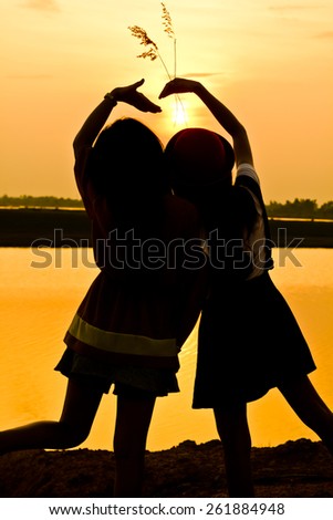 The silhouette of two young girls over beautiful twilight sunset.