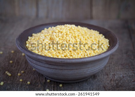 Dry Israeli couscous ptitim in a clay bowl on wooden table. Selective focus: some grains in focus, some are not. Rustic style