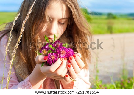 Beauty of nature. Young beautiful girl smelling meadow clover flowers. Summertime outdoors.