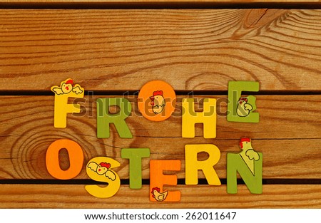 Happy Easter in German. Colorful wooden letters FROHE OSTERN at the bottom of old natural wooden rustic country vintage  brown boards background, close up, top view