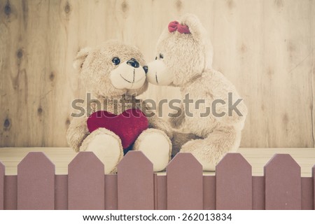 two teddy Bear with Heart on palisade on wood background,vintage tone,concept valentine