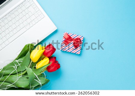 White computer and bouquet of tulips with gift on blue background