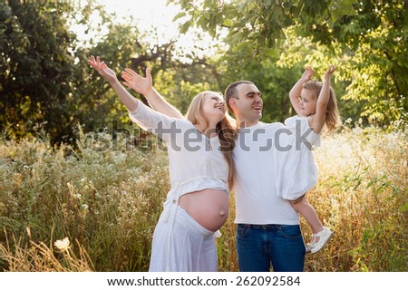 Happy pregnant family having fun in summer nature see and share up
