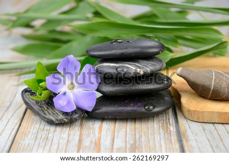 Black warmth zen stones for health piles up on old knotted wooden background with bamboo and purple flower decoration