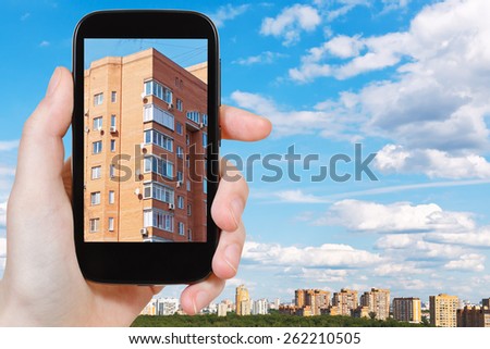 travel concept - tourist takes picture of urban apartment brick house in spring day on smartphone, Moscow, Russia