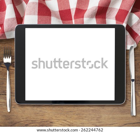 black tablet pc on wooden table with fork and knife