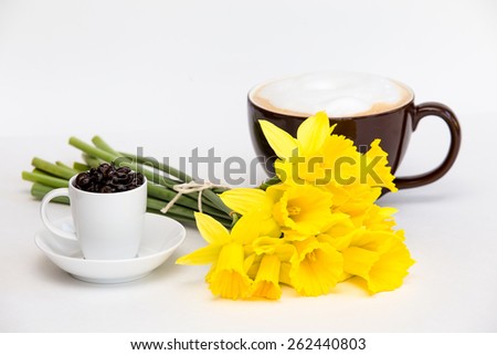 Fun arrangement of coffee beans in cup and saucer with bright and pretty yellow daffodils 
