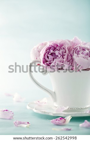 Pink peony flowers in a decorative cup on light blue vintage background with hazy vintage editing