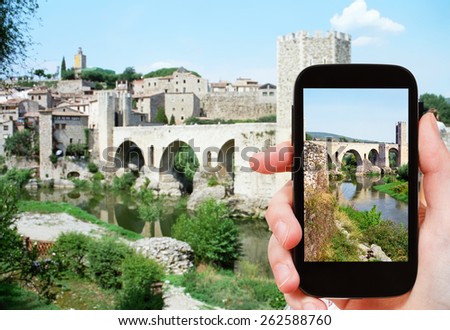 travel concept - tourist shoots photo of 12th-century Romanesque bridge over the Fluvia river in Besalu town on smartphone, Spain