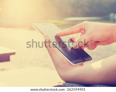 Close up of a woman using mobile smart phone outdoor, nature background. (retro color tone)