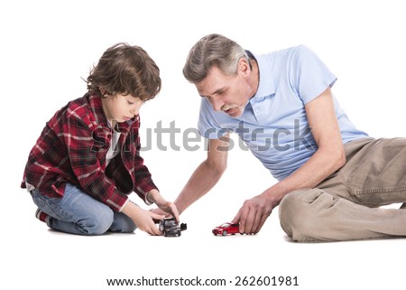 Smiling grandfather and his grandson are playing with cars, over the white background.