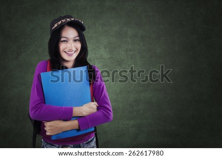 Portrait of modern female student standing in the class while smiling at the camera in front of chalkboard