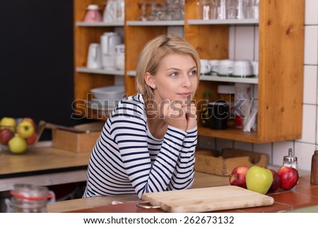 Thoughtful pretty woman with blond hair, wearing stripe long sleeve t-shirt, with hands on the chin, at the kitchen