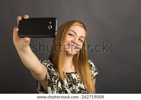 Portrait of cute teenage girl taking self portrait  with her smart phone over gray background