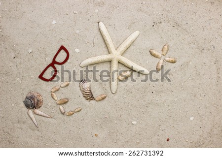 The word RELAX spelled out of seashells and starfish on sandy beach by red sunglasses