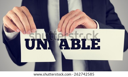Retro vintage style image of a man holding a torn paper sign in his hands with the words - Un - Able- spread over the two halves depicting the concept of opposites. Royalty-Free Stock Photo #262742585