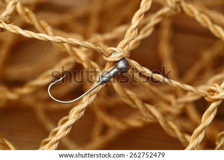 The eye of a fishing hook and the nodes decorative fishing net on blurred background, close up
