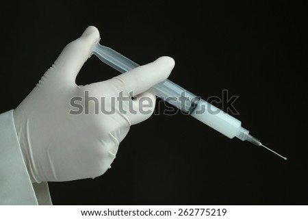 hand with protective glove injecting drug with syringe. dark background.