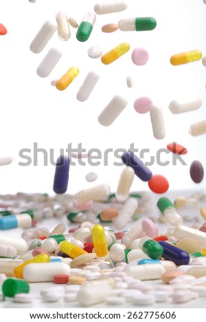 Capsules of colorful remedies falling in white background.