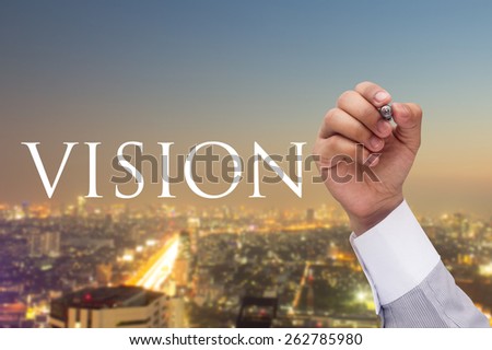 Business man's hand writing massage vision at transparent board on blurred night city background