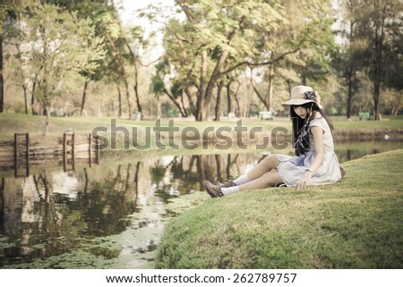 A cute Asian Thai girl is relaxing near the pond in the wilderness in soft vintage color