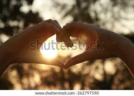 silhouette hand in heart shape with sunlight and flare 