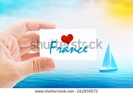 Summer Vacation on France Beach, Person Holding Visiting Card for Summertime Holiday Message Love France and Sailboat at Sea in Background.