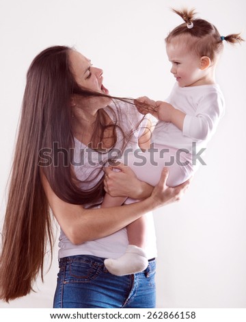 the emotional expressive young  mother with long brown hair in jeans holding a baby who child pulls her mother's hair