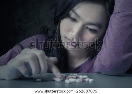 Portrait of teenager girl choosing pills with stressful expression, symbolizing a drugs addict Royalty-Free Stock Photo #262887095