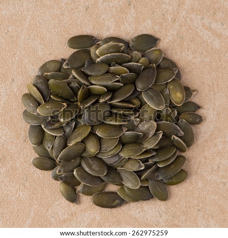 Top view of circle of pumpkin seeds against beige vinyl background.