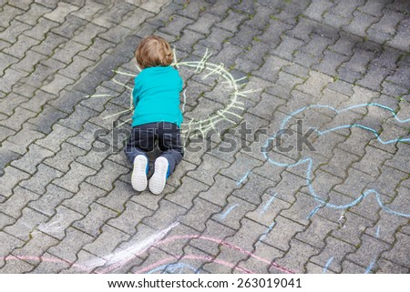 Funny little toddler boy painting sun with colorful chalks outdoors in summer. Kid having fun. Creative leisure with children outdoors.