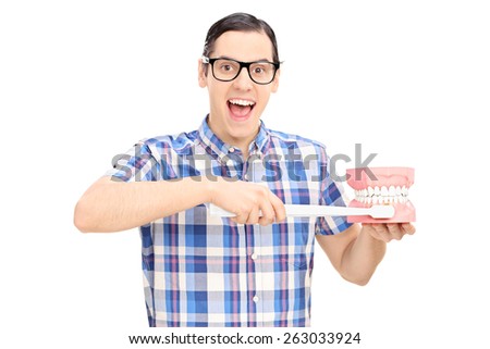 Excited young guy with glasses holding a denture and a toothbrush isolated on white background, studio shot