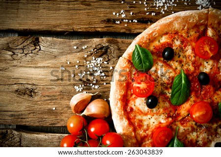 Tasty pizza, tomatoes and others ingredients on a wooden background.  Royalty-Free Stock Photo #263043839