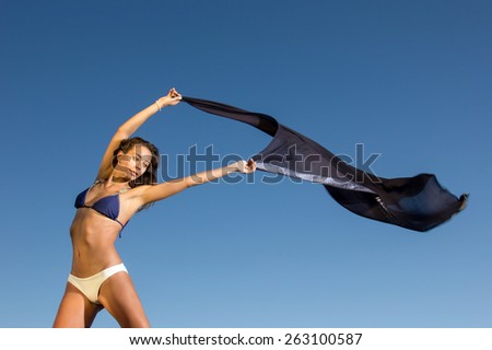 Beautiful young girl with scarf dancing at the beach against the blue sky