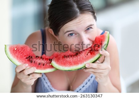 Pretty young woman eating watermelon and looking at the camera. Shallow depth of field. Closeup portrait.