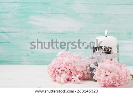 Fresh hyacinths flowers and candle on white wooden background against turquoise wall. Selective focus. Romantic background. Place for text.
