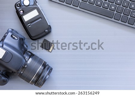 top view of a desktop of a photographer consisting on a camera, a keyboard, a photometer and a memory card on a grey desk background - suitable for copy space