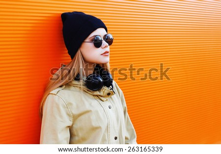 Pretty blonde wearing a black hat and headphones listens to music enjoys freedom, cool hipster girl in the city against a colorful wall, street fashion concept, urban style