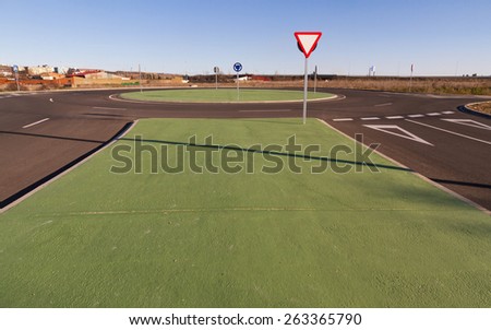 Roundabout roundabout or new construction. Designed to simulate grass green painted cement. Outside urban space. With vertical traffic signs and corresponding asphalt