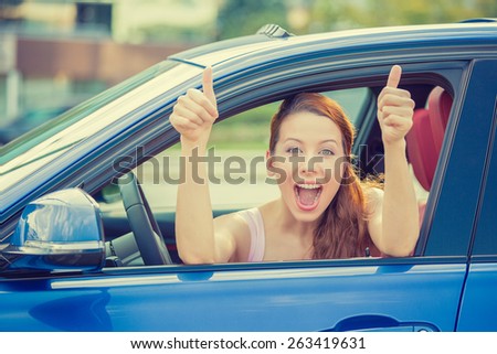 Side door view woman driver happy smiling showing thumbs up sitting inside new blue car  outside on parking lot background. Beautiful young woman happy with her new vehicle. Positive face expression