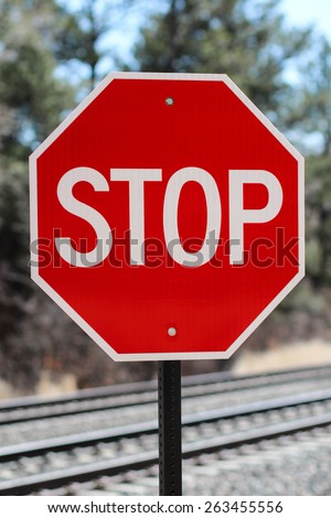 Red And White Traffic Stop Sign Placed Near Train Tracks In Colorado Springs, Colorado Against Forest Background