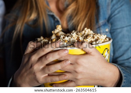 Midsection of woman holding popcorn bucket at cinema theater