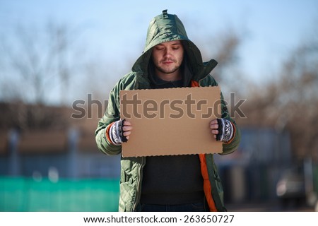 Homeless person with blanck cardboard. Focused on cardboard