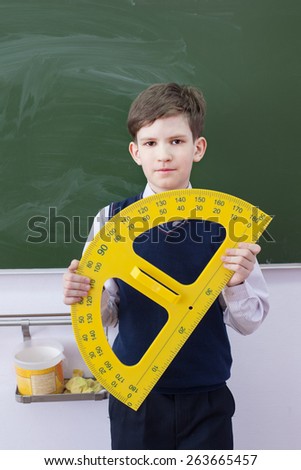 The boy with angle protractor stands in classroom