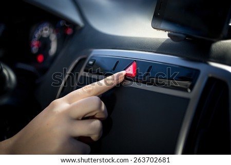 Young woman pressing emergency button on car dashboard 