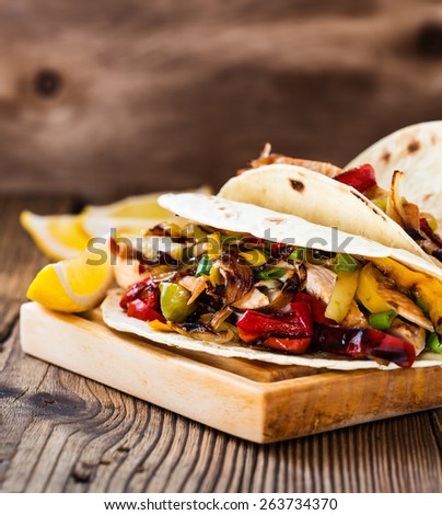 Chicken fajitas with grilled onions and bell peppers and serve with flour tortillas on rural wooden board