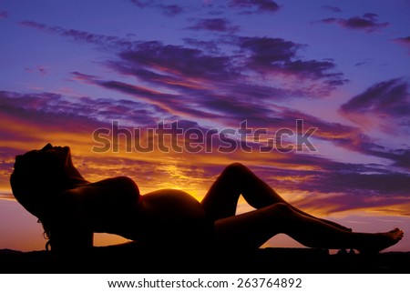 a silhouette of a pregnant woman laying back in the outdoors.